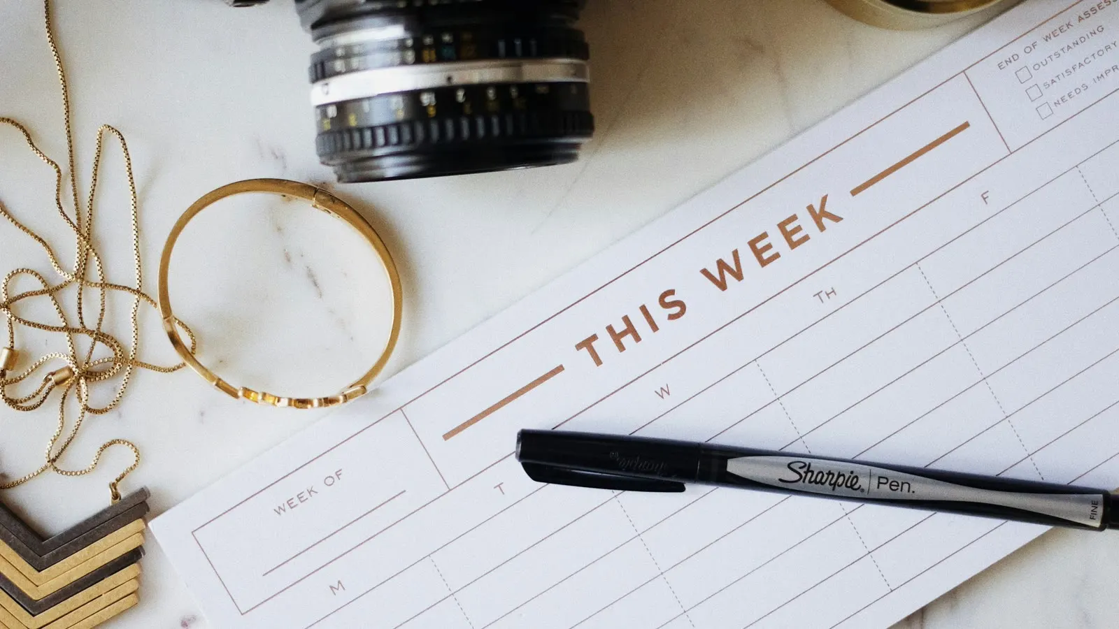 Ett veckoschema bredvid en penna och kamera